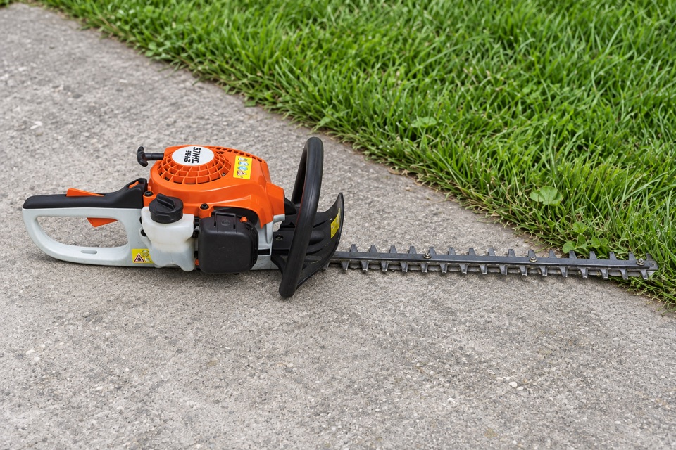 AI illustration of a STIHL hedge trimmer on concrete beside grass