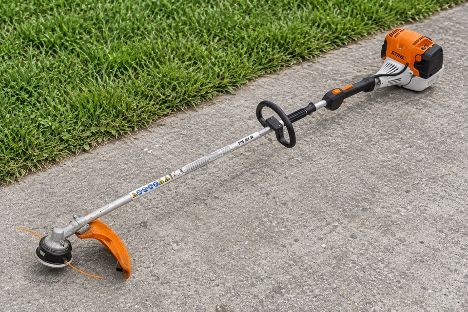AI illustration of a STIHL string trimmer on concrete beside grass